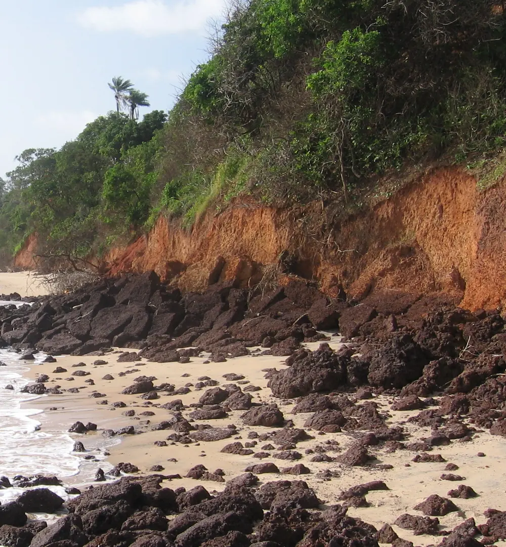 Red clay cliffs covered with green forest above a rocky Atlantic beach at Varela in northern Guinea-Bissau