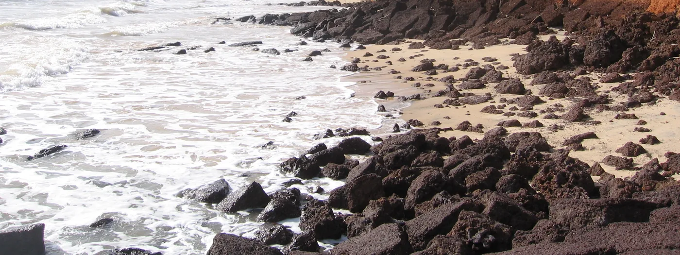 Atlantic surf washing over dark rocks and light sand on the beach at Varela, Guinea-Bissau